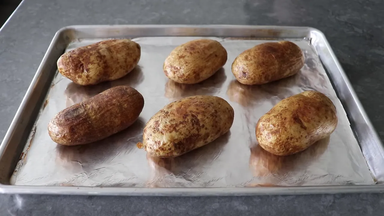 Oiled russet potatoes on a foil-lined baking sheet ready for the oven