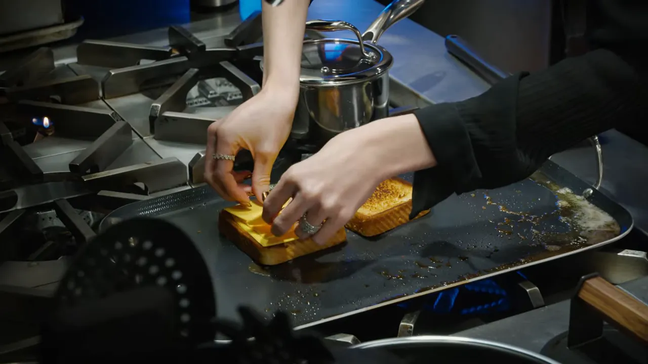 Hands placing cheese slices on bread on a hot griddle