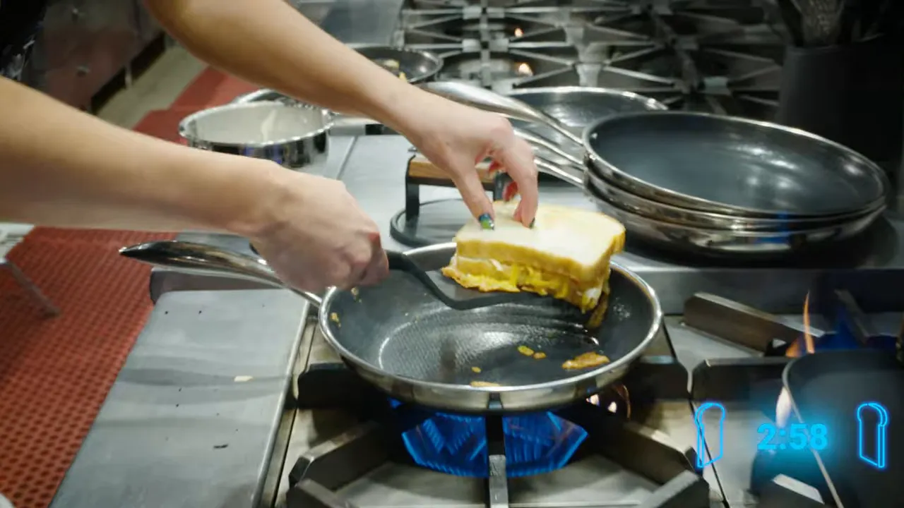 Grilled cheese sandwich being flipped in a skillet over a gas burner