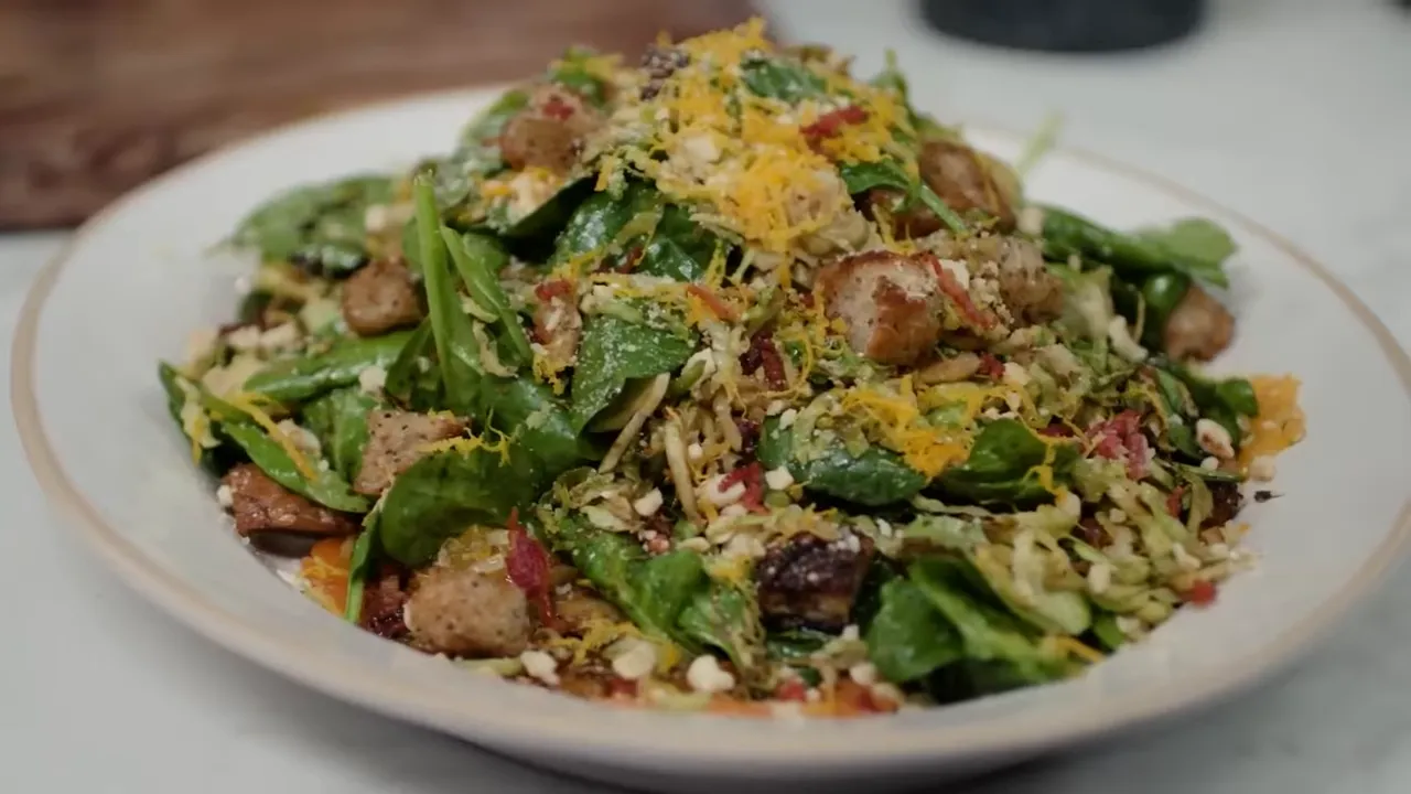 Plated crispy bacon and spinach salad with croutons, shredded sprouts and orange zest