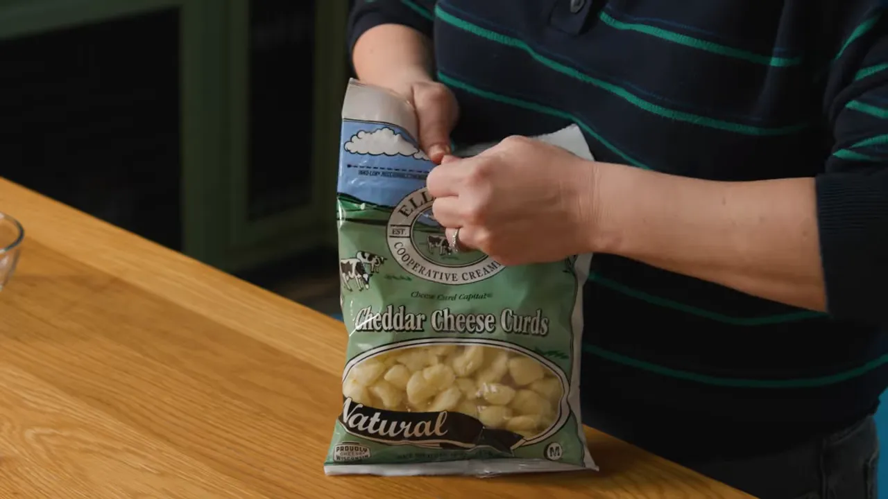 Close-up of hands opening a bag of cheddar cheese curds on a wooden countertop, curds visible through the bag.