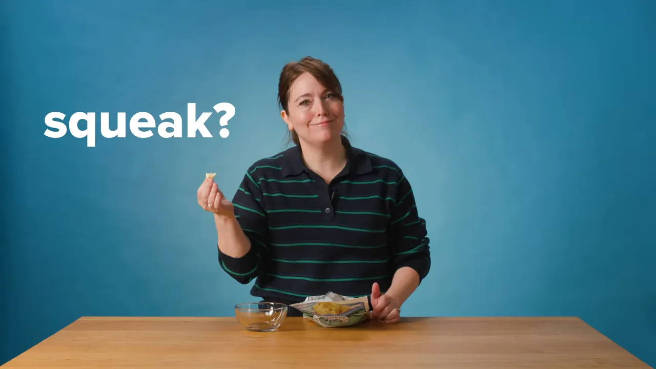 Host holding a cheese curd at a table against a blue background with the word 'squeak?' visible