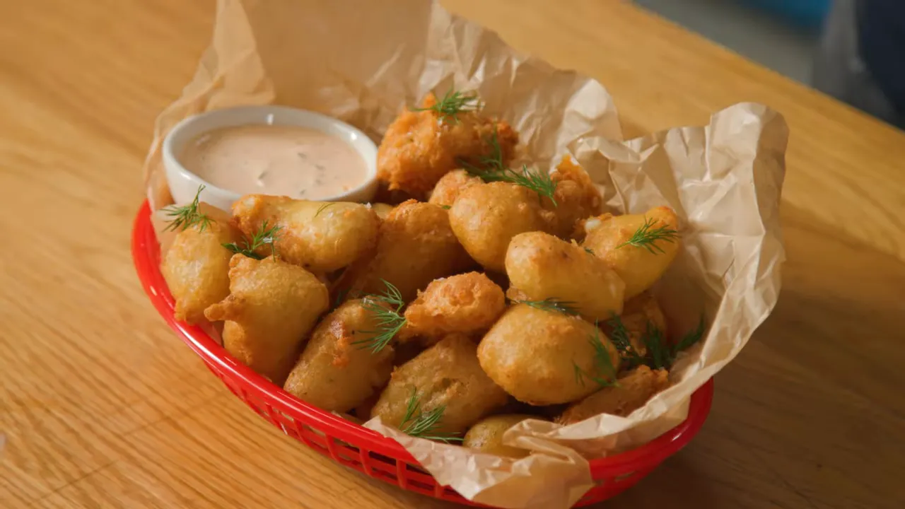red basket of golden fried cheese curds on parchment with a small bowl of dipping sauce