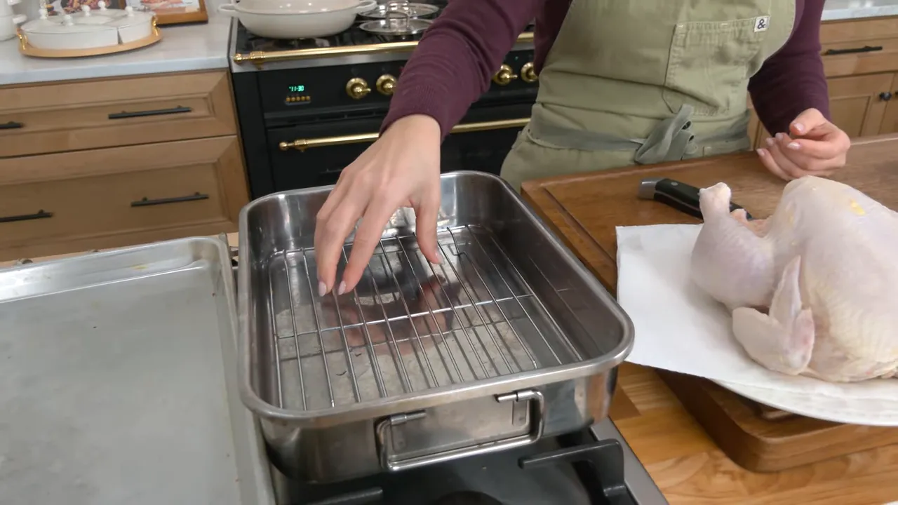 Stainless roasting pan with wire rack and a raw whole chicken on a cutting board beside it