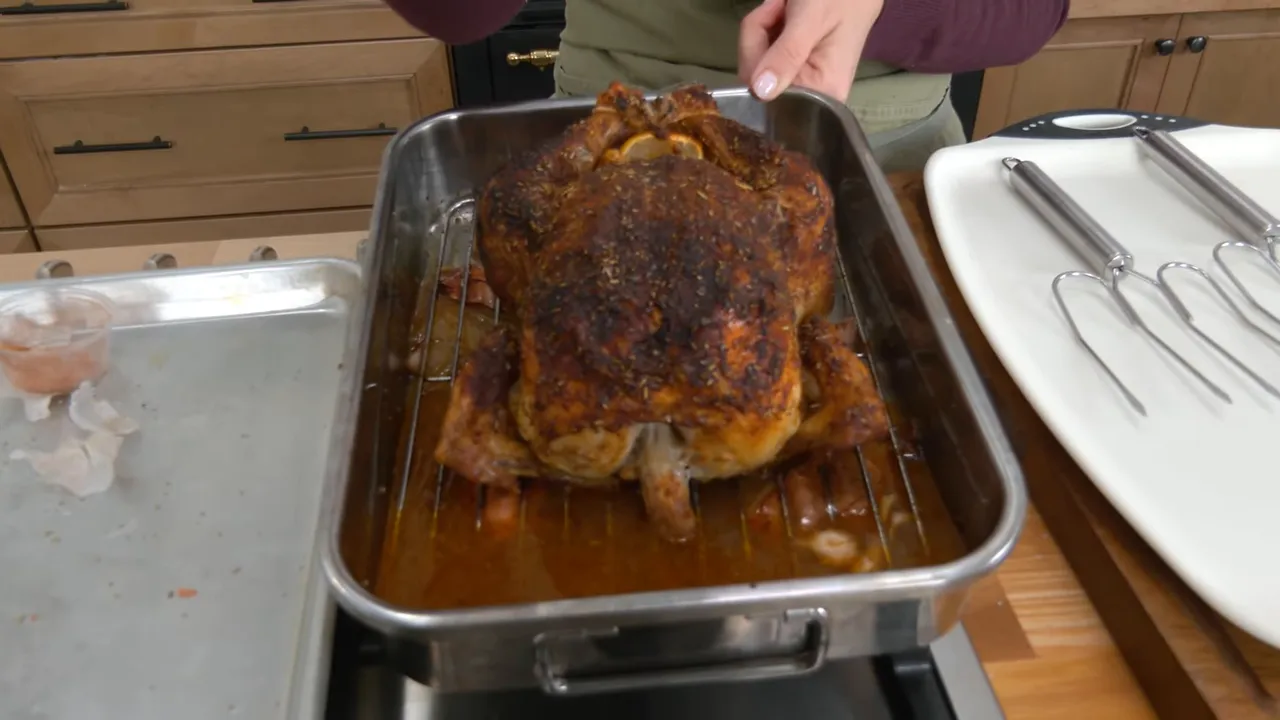 Perfectly roasted whole chicken on a rack in a roasting pan with pan juices and carving forks beside it