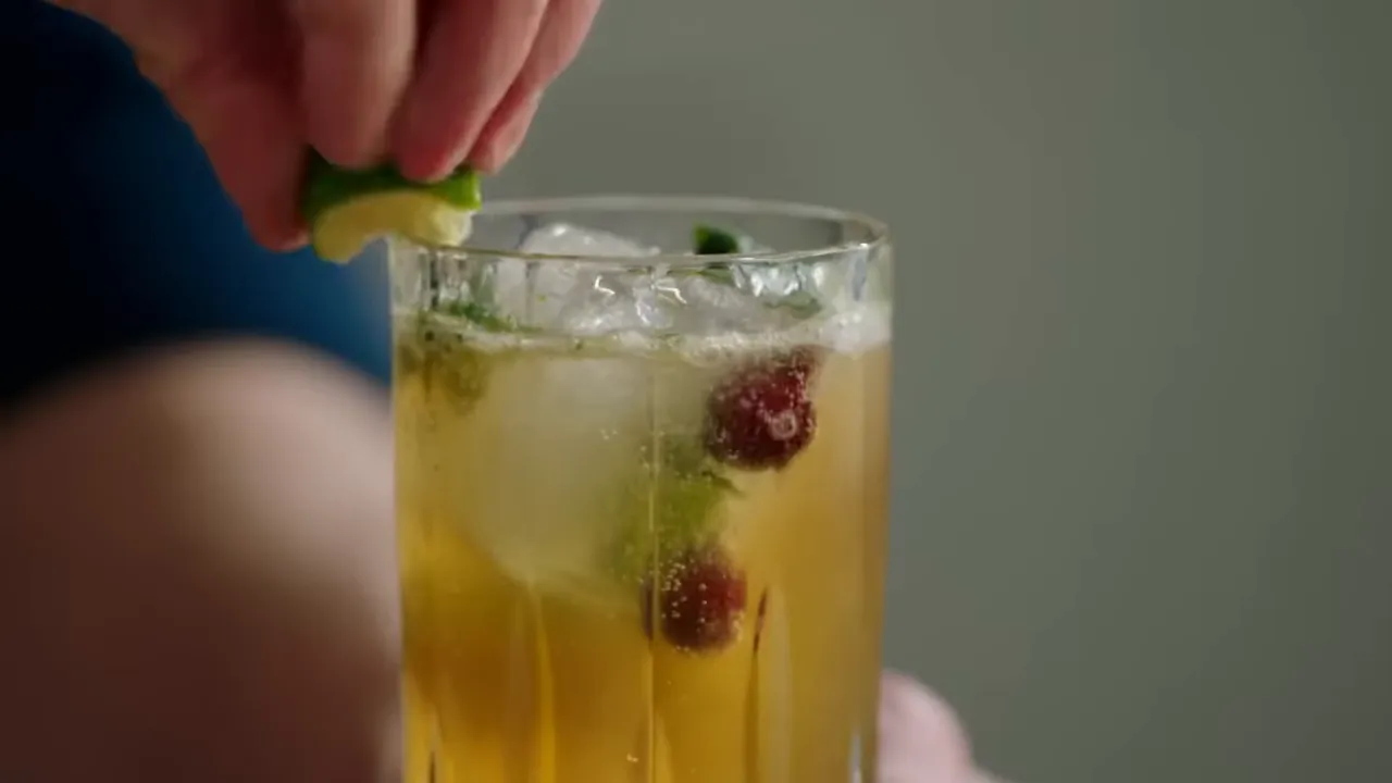Close-up of a sparkling mojito with ice, cranberries and mint as a lime is squeezed over the glass