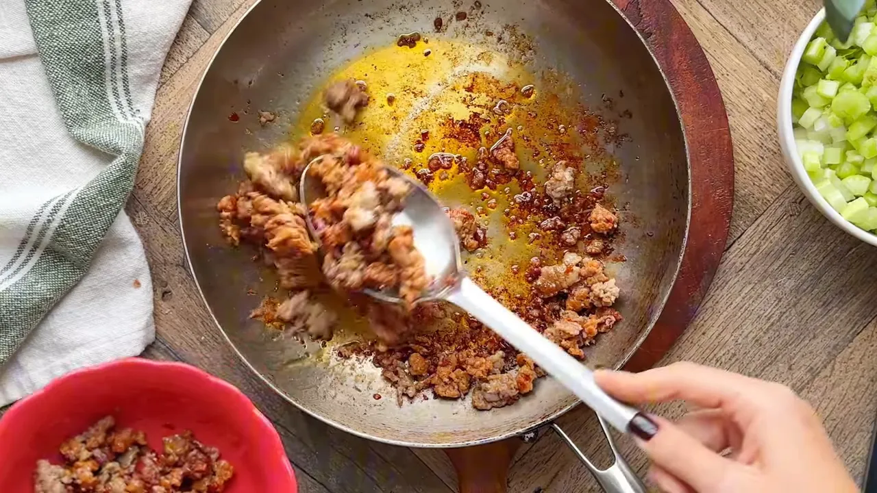 Spoon lifting browned sausage from a skillet into a bowl, skillet fond visible