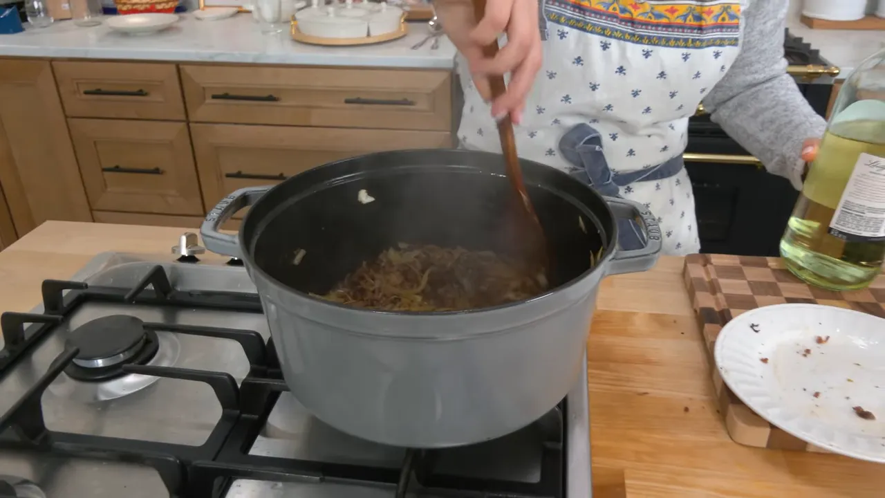 Steam rising from a pot of softened onions and browned meat as they cook in a Dutch oven on the stove.
