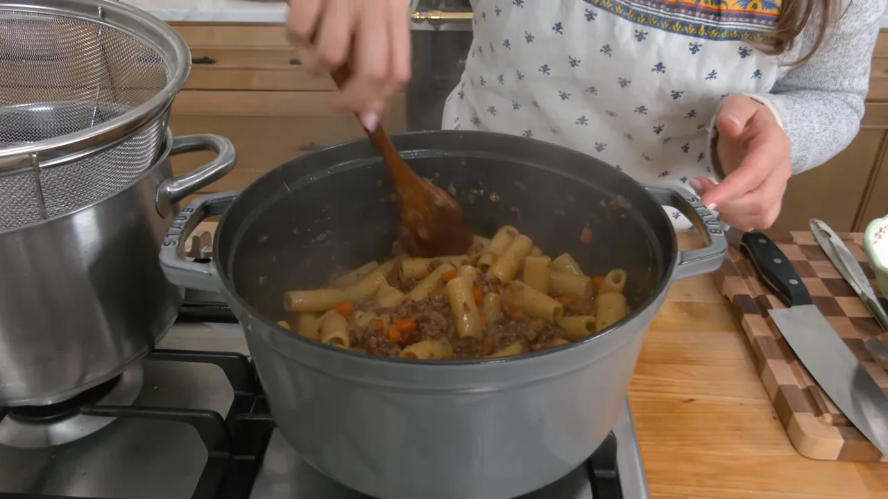 Top-down view of rigatoni simmering in a Genovese onion-and-meat sauce being stirred in a Dutch oven.