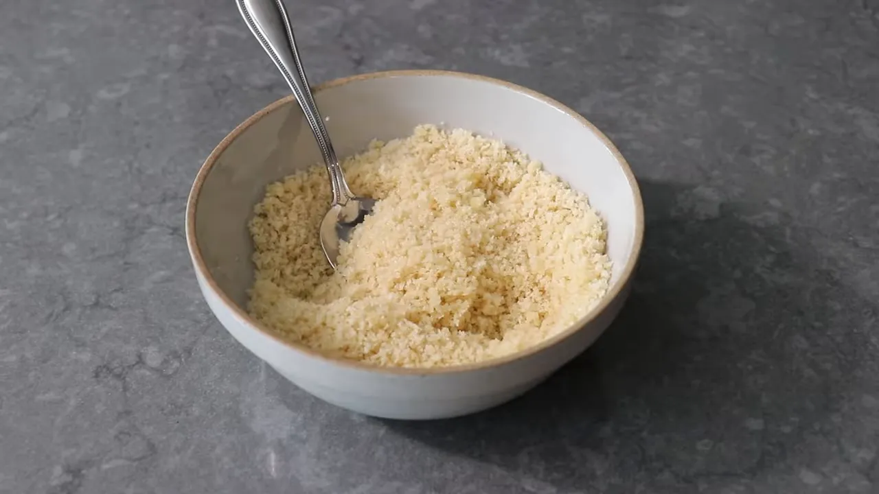 Bowl of buttered breadcrumbs with a spoon, texture like wet sand, ready for topping