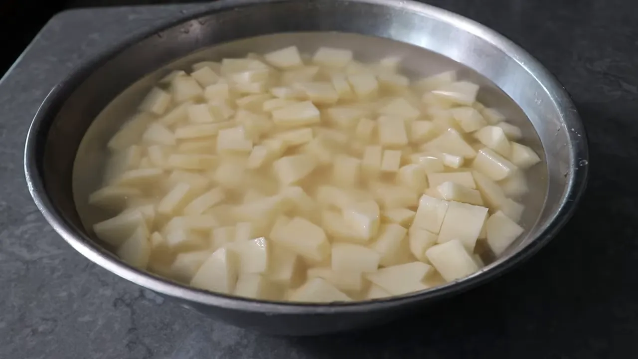 metal mixing bowl of diced potatoes submerged in cold water ready to be drained