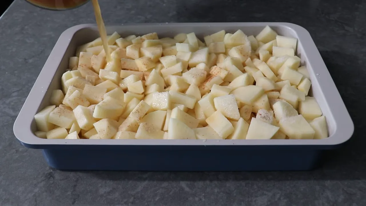 broth being poured into a casserole of seasoned cubed potatoes
