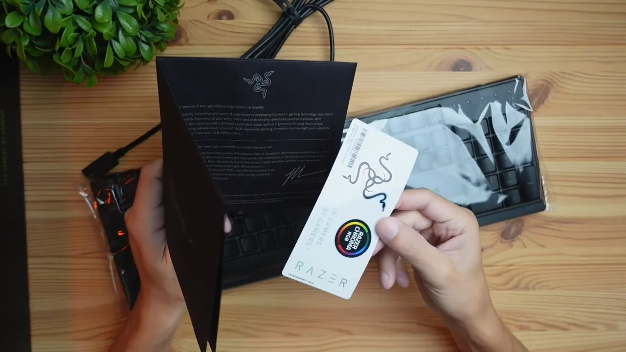 Overhead view of the instruction manual and sticker sheet next to a wrapped Razer Ornata V3 X keyboard on a wooden desk