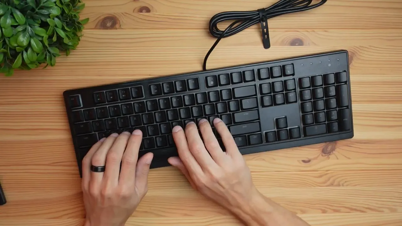 Top-down view of Razer Ornata V3 X keyboard with hands typing on a wooden desk
