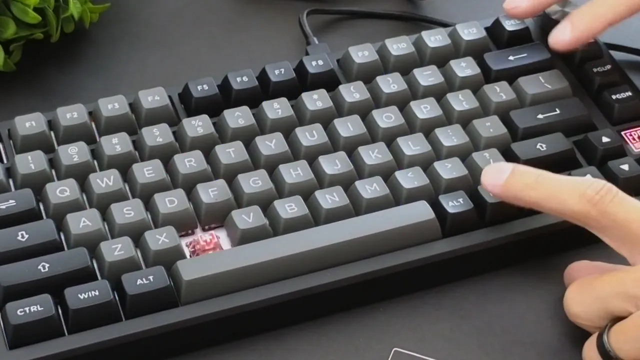Clear close-up of Epomaker TH80 SE keyboard with gray PBT keycaps, visible RGB lighting, a removed key exposing a pink switch, and fingers interacting with the volume knob and keys.