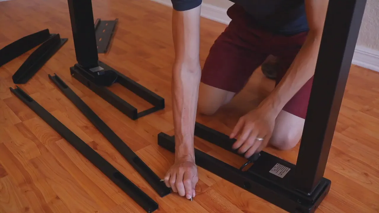 Hands tightening bolts and aligning the standing desk's leg components on the floor during assembly