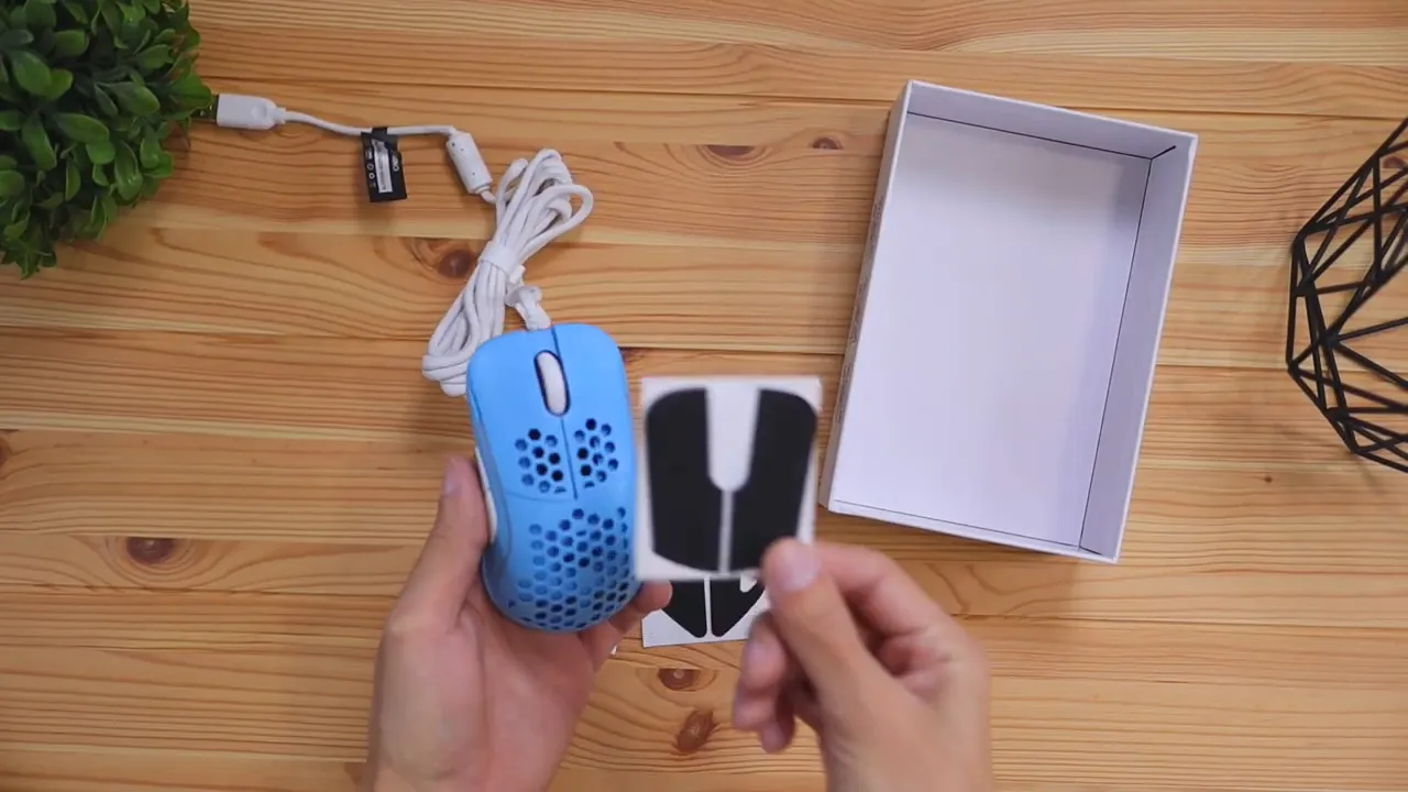 Blue gaming mouse held above a desk with extra black grip stickers and open box nearby