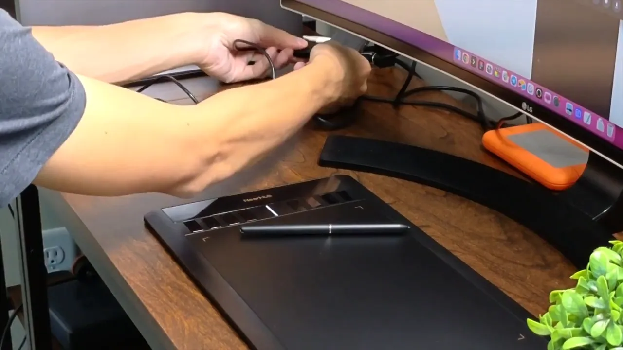 Hands plugging USB cable into computer next to NEARHUB S13 tablet and monitor