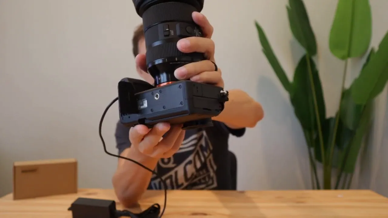 Clear bottom view of a Sony A7IV with the battery compartment open and the dummy battery cable routed out to the power brick.