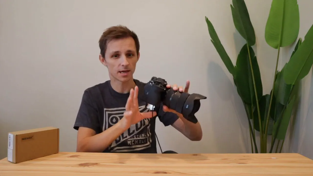 Sony A7IV held by presenter with dummy battery visible in open battery compartment and cable attached