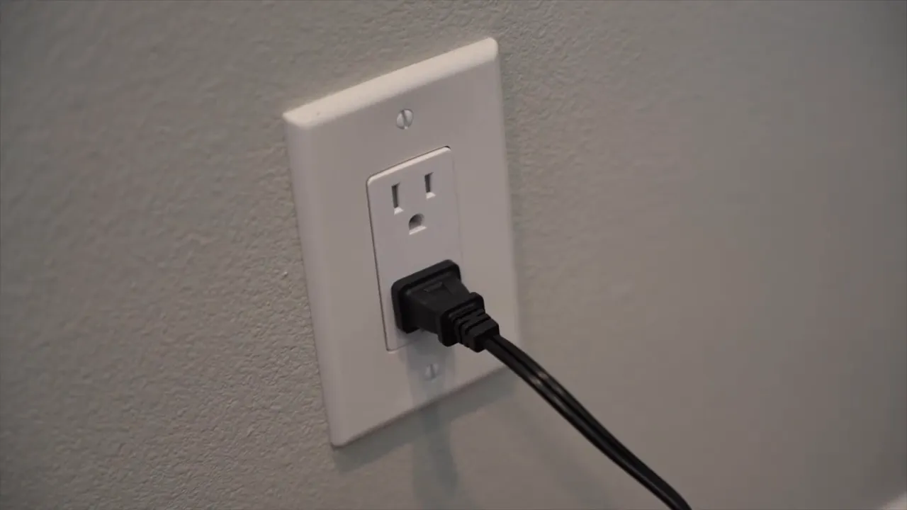 Close-up of an AC power plug inserted into a wall outlet, powering a dummy-battery power brick.
