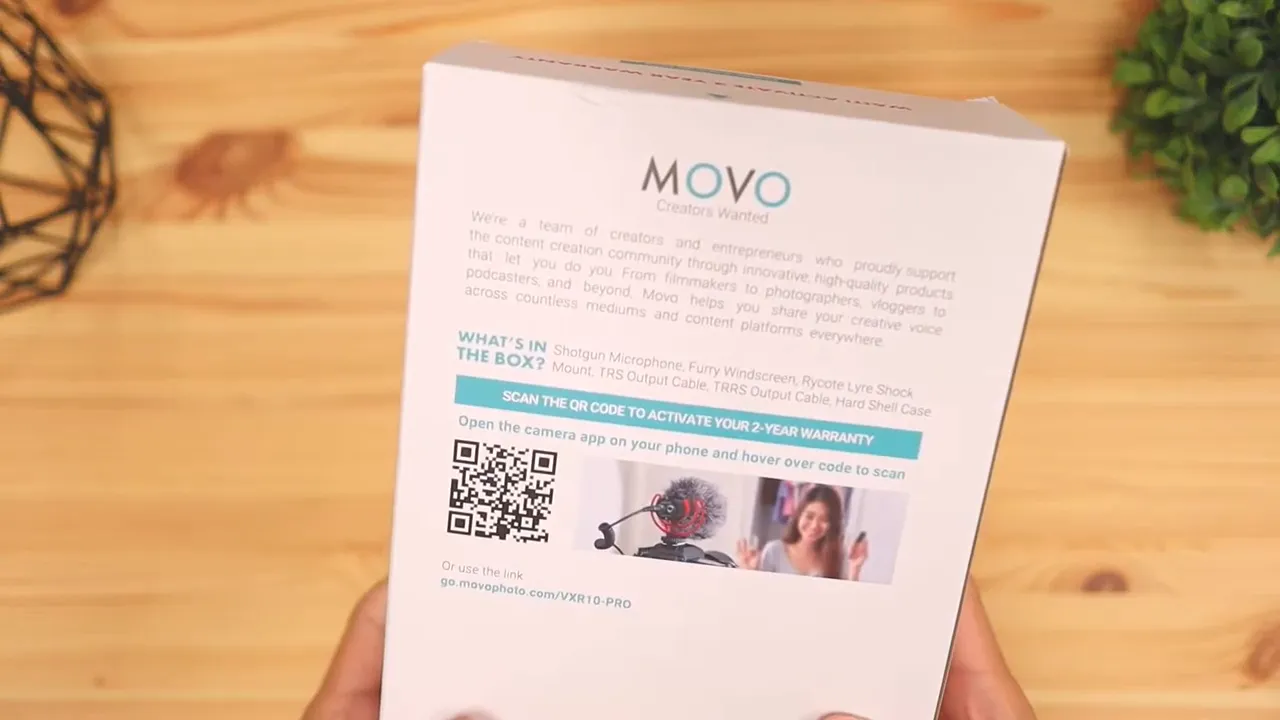 Hands holding the Movo microphone with foam windscreen attached over a wooden table