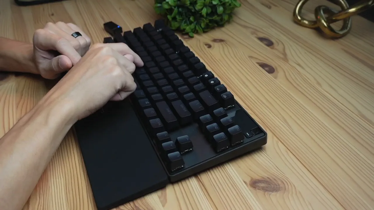 Close-up of hands typing on the SteelSeries Apex Pro TKL keyboard with wrist rest on a wooden desk