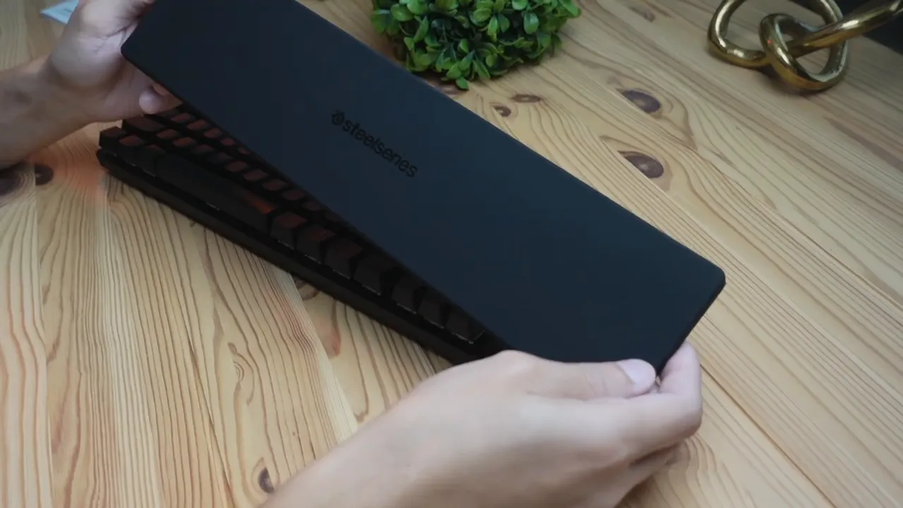 Hands placing the SteelSeries Apex Pro TKL magnetic wrist rest onto the keyboard on a wooden desk
