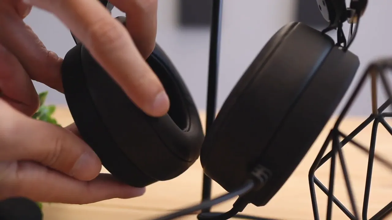 Hand pressing the soft ear cushion of the Nubwo N7 while the headset hangs on a stand