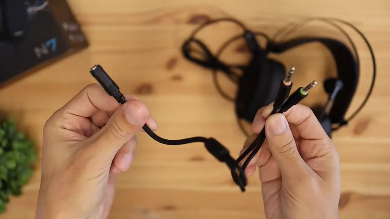 Hands holding the headset splitter cable with single and dual audio connectors over a wooden desk