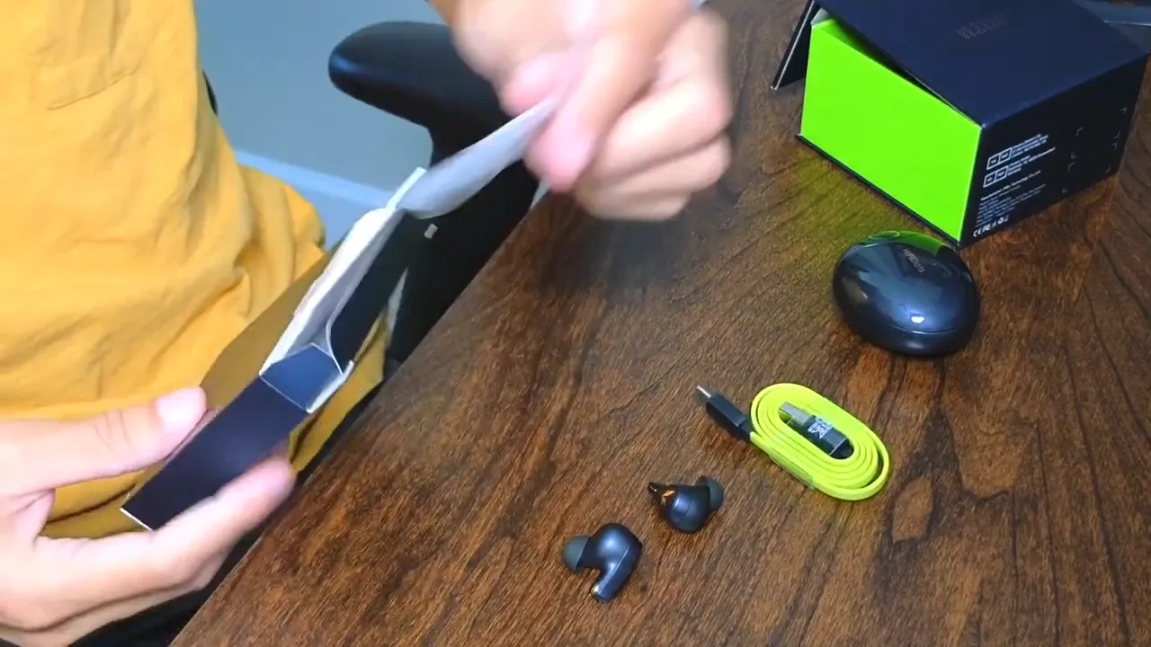 Unboxed Mifo HiFiDots: two earbuds, charging case, lime short charging cable and packaging laid out on a wooden table