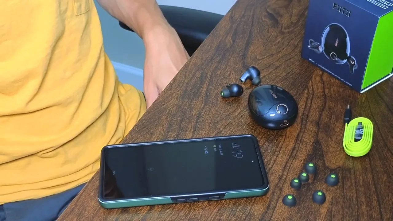 Mifo HiFiDots earbuds, charging case, extra ear tips and a smartphone laid out on a wooden table for a call test