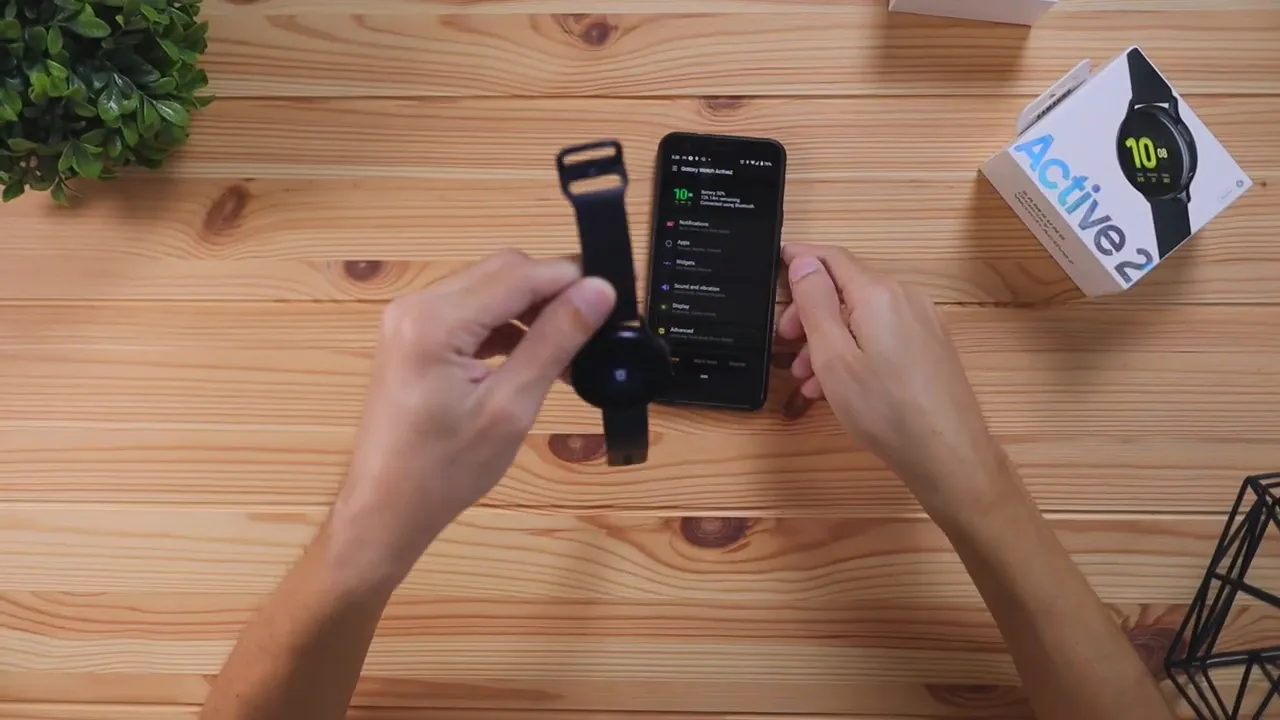 Hands placing the Samsung Galaxy Watch Active 2 strap while the Galaxy Wearable app is on the phone screen