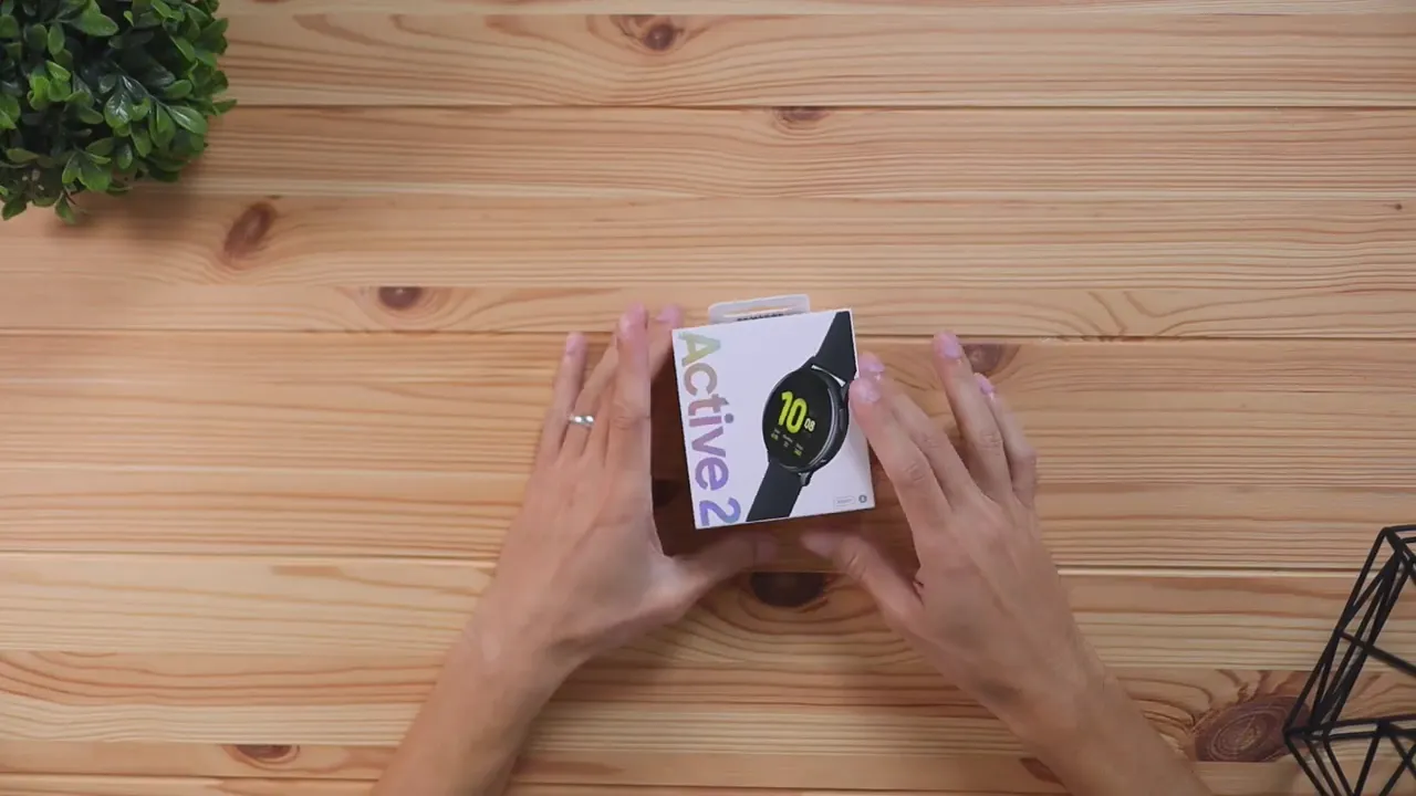 Hands holding the Samsung Galaxy Watch Active 2 retail box on a wooden table