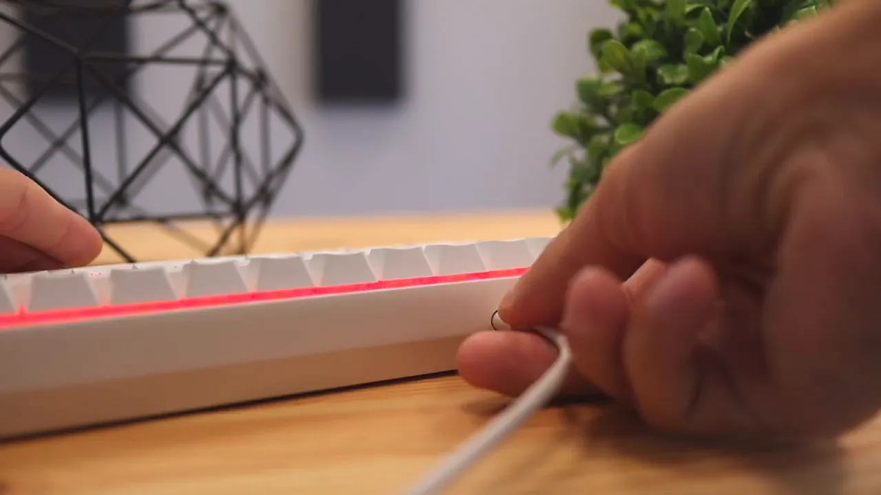 White keyboard with USB C cable plugged into the side and red lighting active