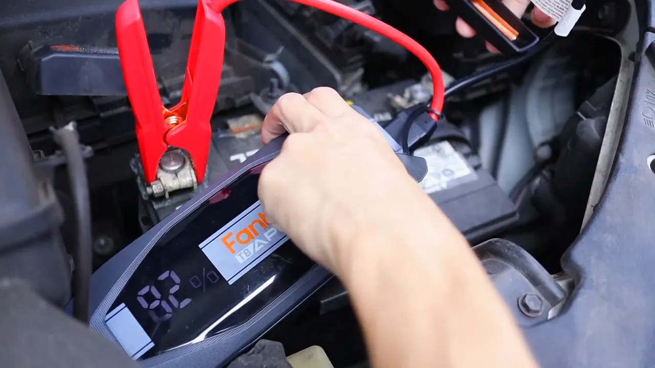 Red jumper clamp clipped to the battery positive terminal with the FANTTIK T8 APEX display visible