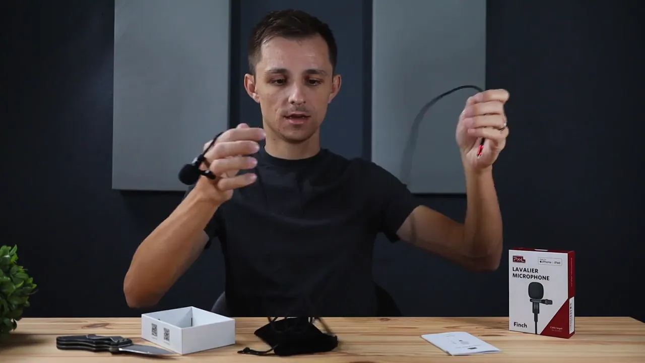 Hands holding a Pixel Finch lavalier microphone with the cable extended and the product box visible on the table