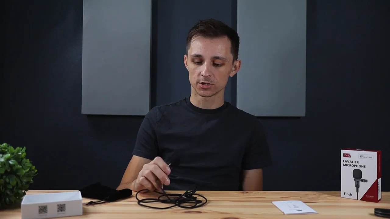 Host looking down and handling the Pixel Finch lavalier cable on the table — demonstrating a short pre-recording test.