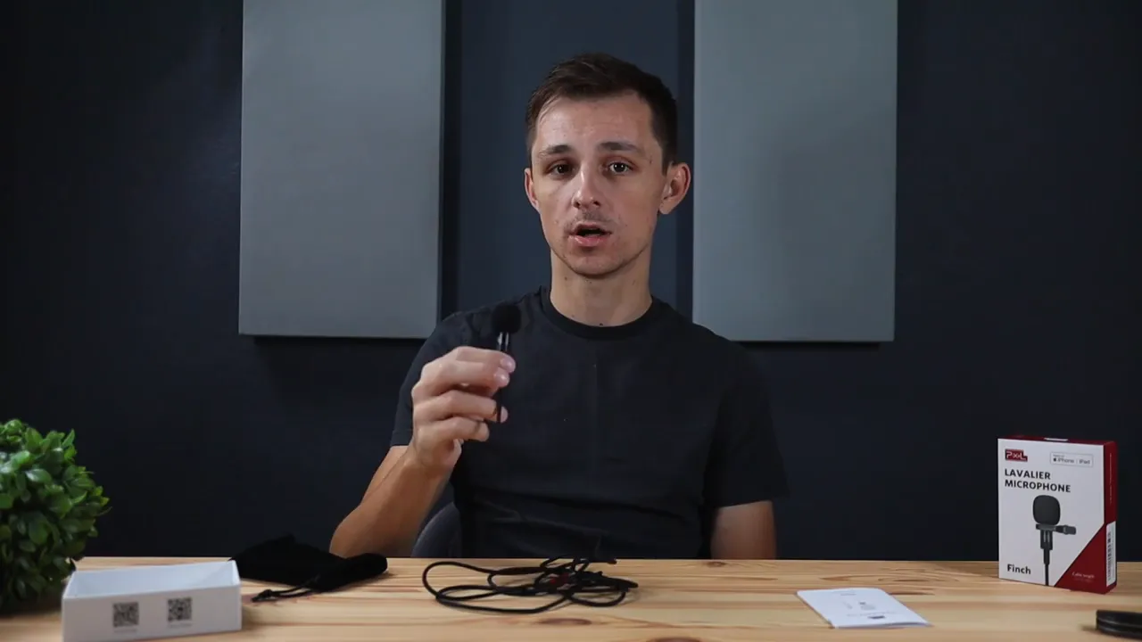 Presenter holding the Pixel lavalier microphone up close with cable and Pixel box on the desk.