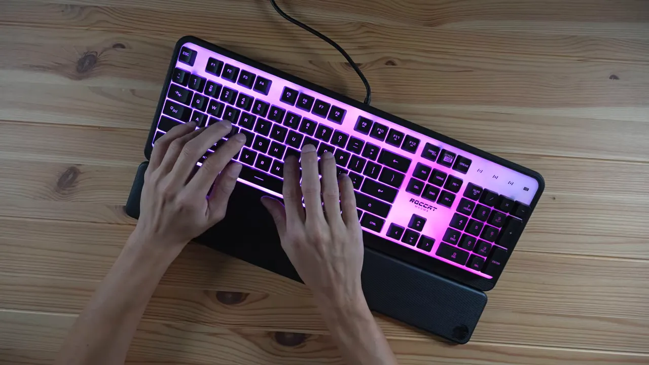 Top-down view of Roccat Magma keyboard with both hands typing and a pink/purple RGB backlight.