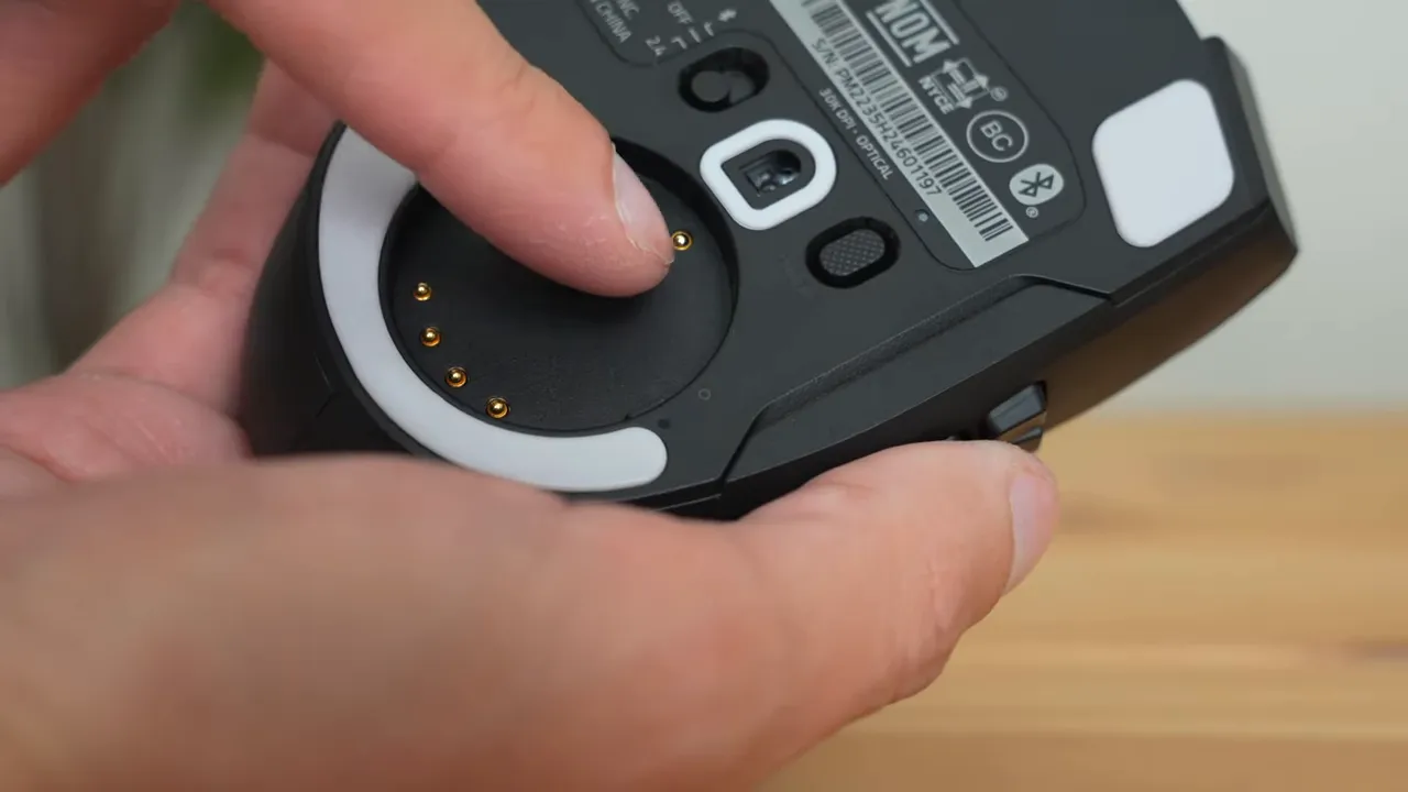 Razer Naga V2 Pro underside with twist-off ring removed showing gold contact charging pins and mode switch