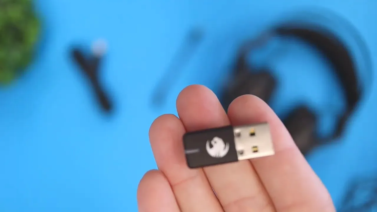 USB wireless receiver dongle held in a hand with headset blurred in background