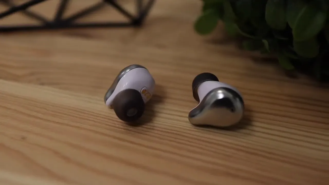 Two Mifo earbuds resting on a wooden desk showing the rounded stemless shape and reflective outer shell