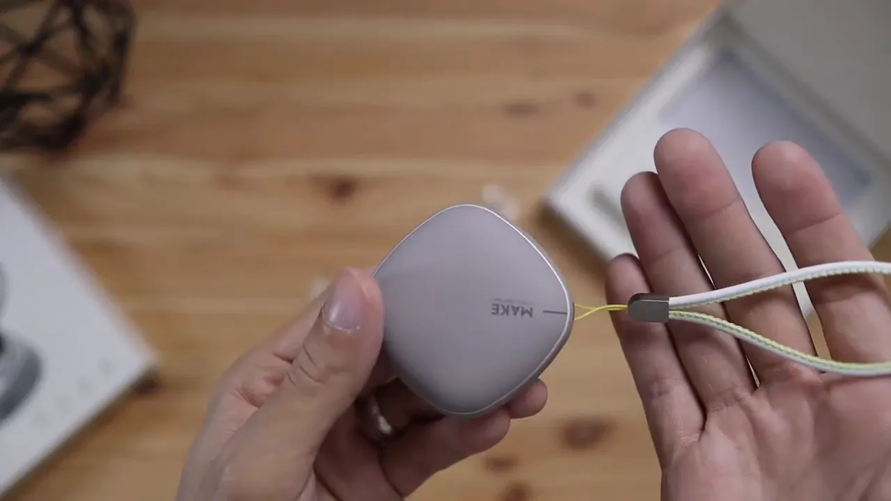 Hand holding the gray square-shaped Mifo charging case with braided loop attached