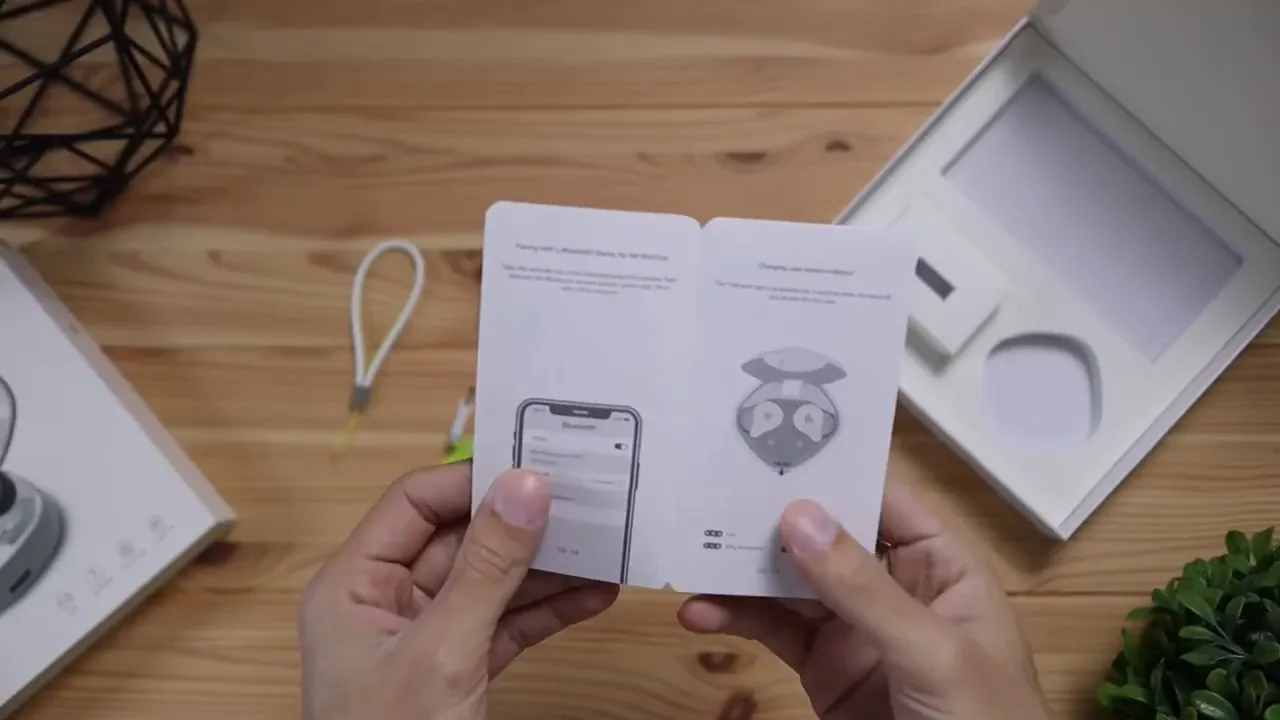 Open quick start guide held above a wooden desk with illustrations for phone pairing and earbud functions