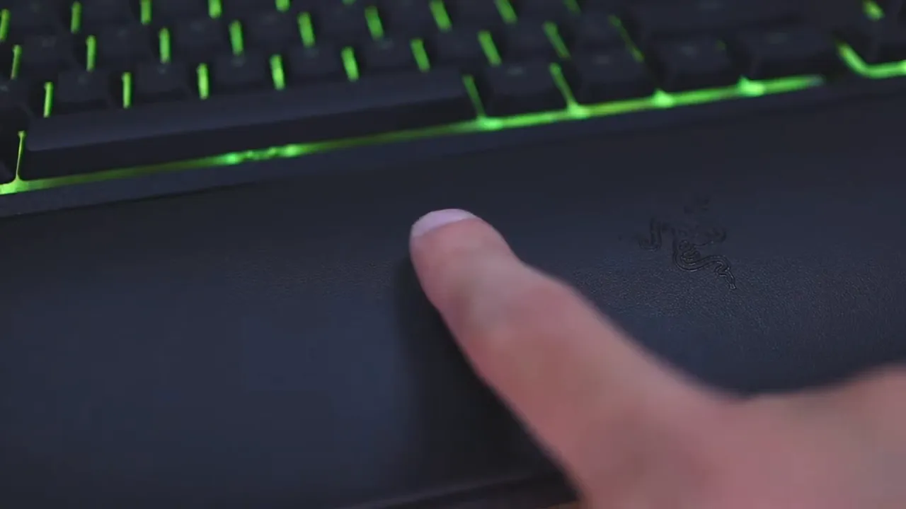 Finger pressing into the Razer wrist rest in front of the keyboard with green lighting