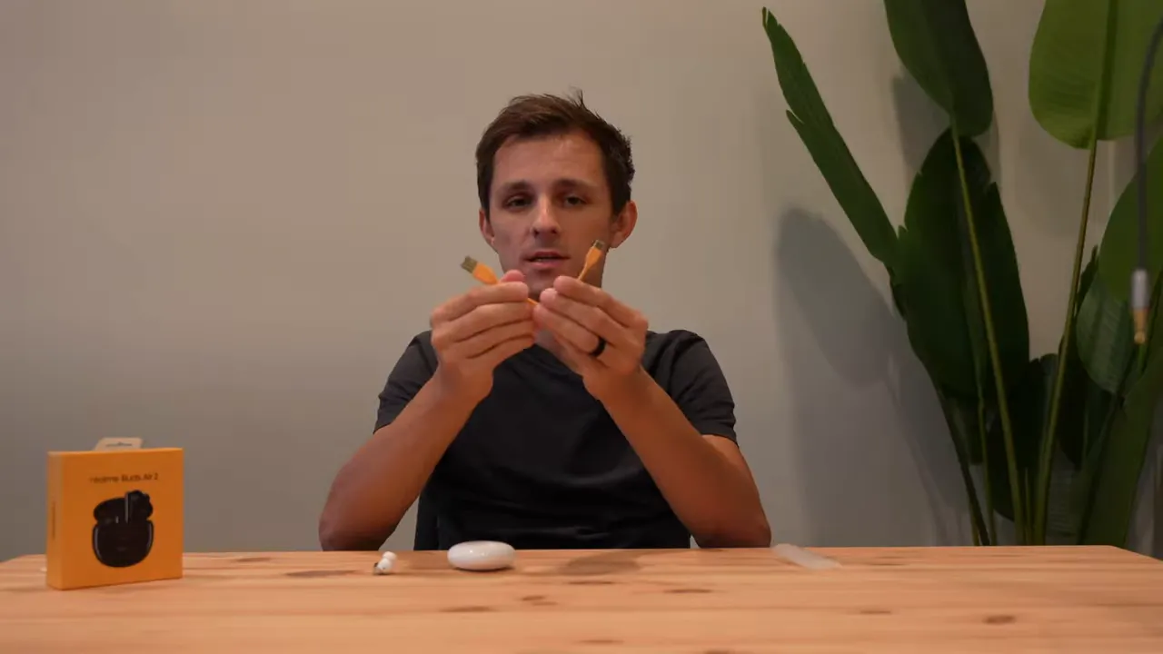 Presenter holding the included yellow USB-A to USB-C charging cables with the Realme Buds Air 2 case on the table