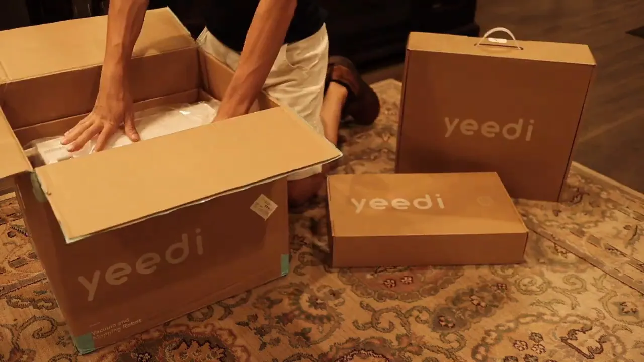 multiple Yeedi product boxes on a rug with hands unpacking components