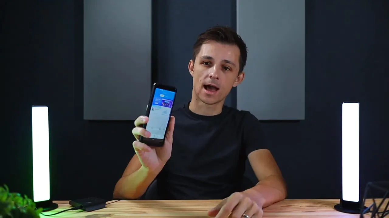 Smartphone showing the Govee Home app during setup, held up by the presenter between two LED light bars.