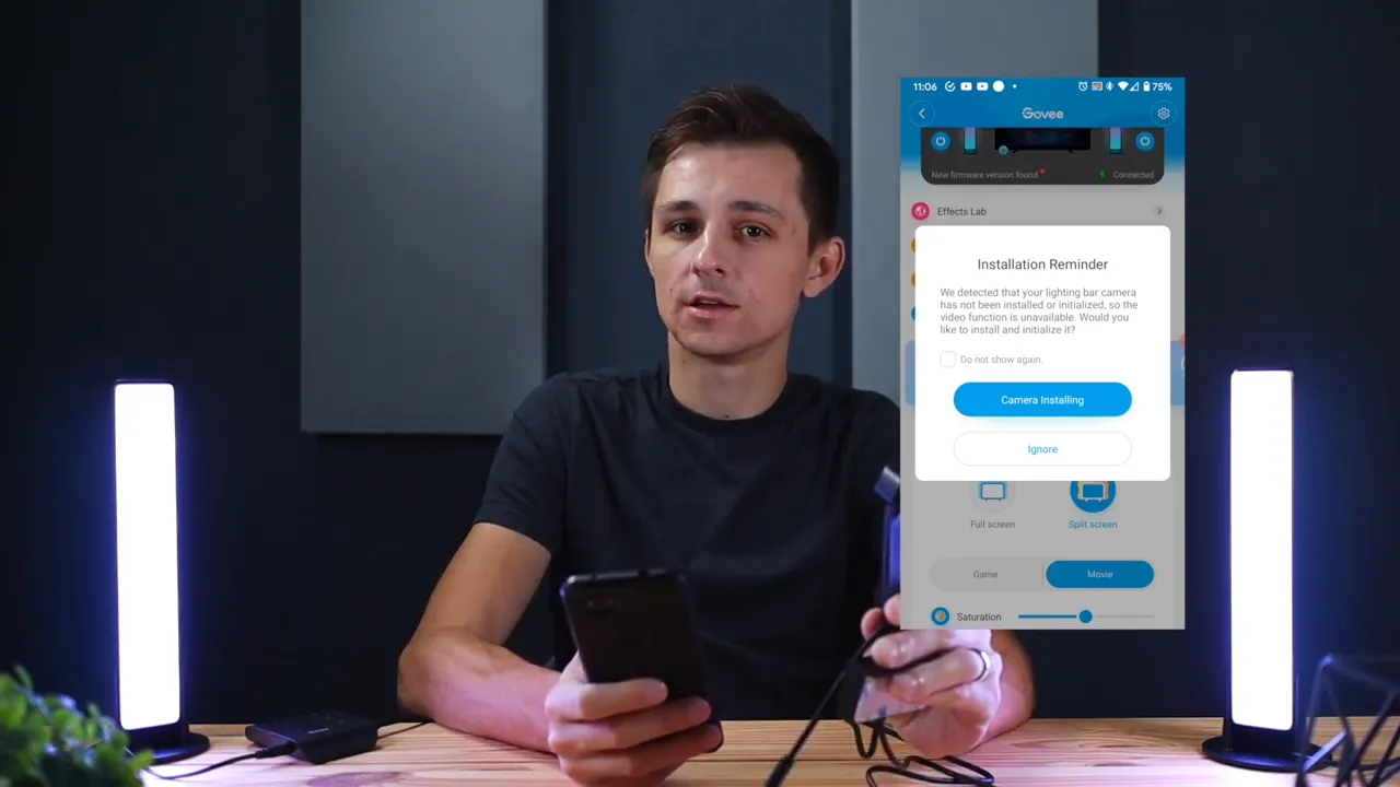 Presenter holding the Govee camera and cables on a table with the Govee app installation reminder visible and LED light bars lit.